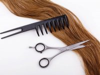 Steel scissors lie on the wave of silk brown hair with a black comb